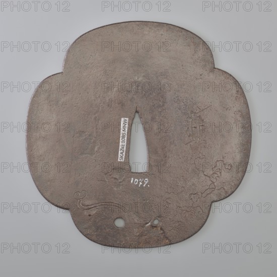 Crossguard tsuba, Kaneie; craft: tsuba; maker/school: Kaneie; gift; Japanese; Edo 1603–1868; 18th century; Fushimi, Yamashiro, Japan; full, four-leaf tsuba; inlay with shakudo and gold; motifs: scrolls, calligraphy, Buddhism, Zen Buddhism, monks, Daruma mythology; function: sword crossguard for katana; diameter: 11.3 cm., A roughly clover-shaped metal object with a central tapered opening and two round holes near one edge, showing a worn, textured surface in shades of brown and gray with darker brown and rusty areas; faint incised decorative lines and subtle raised bumps appear on the surface, and the background is a smooth pale gray.