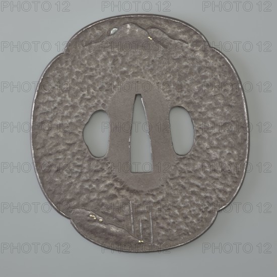 Crossguard tsuba, attributed to Kaneie craftsman/school. Tsuba in the shape of a quatrefoil mokkô gata with a slightly raised edge uchi kaeshi and ryôhitsu ana, textured surface ishime ji. Decorated in low relief hirabori with a landscape motif: a fisherman sitting on the water's edge under a cliff, moon emerging from behind distant hills; motifs include rocks, mokkô, bamboos, trees, mountains. Signed. 18th century Edo period, 1603–1868, Japan — Fushimi, Yamashiro. Materials/genre: Japanese sword crossguard tsuba. Dimensions: height 8.5 cm; width 7.8 cm; depth 0.4 cm., A roughly oval, slightly scalloped metal object with a textured, dimpled surface in shades of dark gray and muted silver sits against a pale gray background; it has three central openings with smooth edges and a vertical central cutout flanked by two rounded cutouts, and small brighter silver highlights along the rim and inside the cutouts; a few tiny gold-colored flecks are visible near one scalloped edge and another sm...