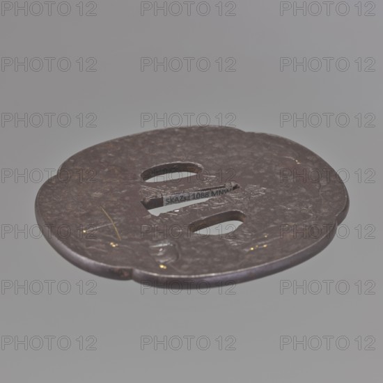 Crossguard tsuba, Kaneie craftsman, Japanese, Edo period 1603–1868, 18th century. Tsuba in the shape of a quatrefoil mokkô gata with a slightly raised edge uchi kaeshi, textured surface ishime ji and ryôhitsu ana. Decorated in low relief hirabori with a landscape motif: a fisherman sitting on the water's edge under a cliff, moon emerging from behind distant hills; motifs include rocks, mokkô, bamboos, trees, mountains. Signed. Place of origin: Fushimi, Yamashiro, Japan. Materials/function: sword crossguard for katana. Dimensions: height 8.5 cm, width 7.8 cm, depth 0.4 cm., A round, flat metal object with an irregular edge and a weathered surface in shades of brown and dark gray, showing a few shallow depressions and scratches and small spots of gold-colored wear; it has a pair of rounded rectangular cutouts and a central slot, and sits against a smooth pale gray background.
