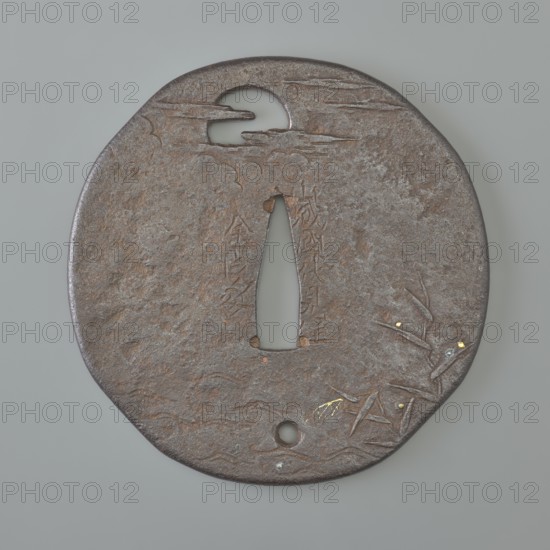 Crossguard tsuba, Kaneie,  school craftsman author. Japanese iron oval tsuba with an irregular outline slightly merging into a quatrefoil mokkô, slightly marked edge uchi kaeshi, textured surface. Decorated in low relief with details inlaid with gold and cut into negative openwork. Both sides show waterside reeds and a full moon emerging from behind clouds. One hole udenuki ana at the bottom. Signed. 18th century Edo period, 1603–1868. Japan; Fushimi, Yamashiro. Materials/subject: Japanese art; moon iconography; weapons—swords, katana; sword crossguards, tsuba. Dimensions: height 7.7 cm, width 7.6 cm, depth 0.3 cm., A roughly circular metal object with an irregular edge sits against a pale gray background; the metal surface is dark brown with areas of reddish-brown and subtle gray patina, and shows a textured, pitted finish. Near the top is a crescent-shaped cutout with cloudlike incised lines extending from it, and a tall narrow central opening runs vertically toward the middle. A few...