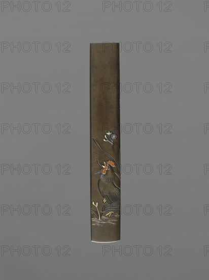 Knife handle kozuka, Suiyôdô, Toshimasa,  craftsman; Japanese; Edo 1603–1868, 19th century; materials/genre: weapons, bladed weapons, swords, katana, kozuka; subject/iconography: flowers, roosters; dimensions: height 9.6 cm, width 1.4 cm; ., A tall, narrow rectangular object with a smooth, dark brown surface stands vertically against a solid gray background; near the lower portion there is an embossed decorative scene showing a bird with textured feathers in shades of dark brown and black, with small accents of orange on its head and beak, standing among stylized plants rendered in muted gold and silver tones, and a few delicate floral elements in silver near the bird, all set above subtle horizontal marks suggesting water.