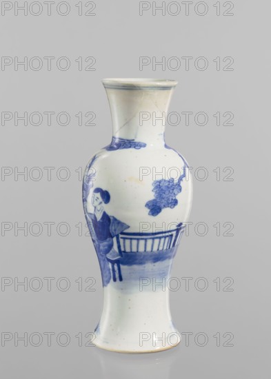 Vase, figurative scenes; ceramics; Chinese art; Chinese culture; blue-and-white porcelain; terraces architectural motif; origin: China; Qing dynasty 1644–1911; porcelain vase with transparent blue-gray glaze and underglaze cobalt painted decoration; 19th–20th century; vessel; height 24.3 cm; diameter 9 cm., A slender porcelain vase with a flared mouth and foot sits against a neutral gray background; the vase is primarily white with blue painted decoration showing a seated human figure beside a railing and foliage, with additional blue brushwork around the neck and lower body, and small flecks and subtle discolorations visible on the surface.