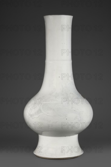 Vase, Chinese, Qing dynasty 1644–1911, 19th century. Porcelain body, spherical, flattened horizontally on a high foot; high, wide neck with a rim. Decoration: dragons engraved under the glaze into the body and filled with cobalt. Height 42.7 cm; diameter 21.5 cm., A tall bulbous ceramic vase with a long cylindrical neck and a flared foot, rendered in white with very faint pale gray decorative motifs visible on the rounded body, sitting against a dark gray background; the vase surface shows a few small dark specks and subtle irregularities in glaze, and the rim and base edges reveal a thin darker brownish-gray line.