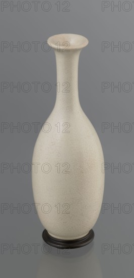 Vase on saucer. Vase made of stoneware or thick porcelain?, ovoid with a long cylindrical neck flaring at the spout; light cream white matte glaze covered with fine cracklework. 19th century, Japan, Edo 1603–1868. Ceramics, bottles. Height 24.1 cm, diameter 8.6 cm, weight 0.65 kg., A tall, narrow-necked vase with an elongated bulbous body stands on a low round base; the vase surface shows a fine network of hairline crackle patterns and is an off-white or cream color with subtle warm beige variations, while the base appears dark brown to nearly black. The background is a smooth, muted gray.