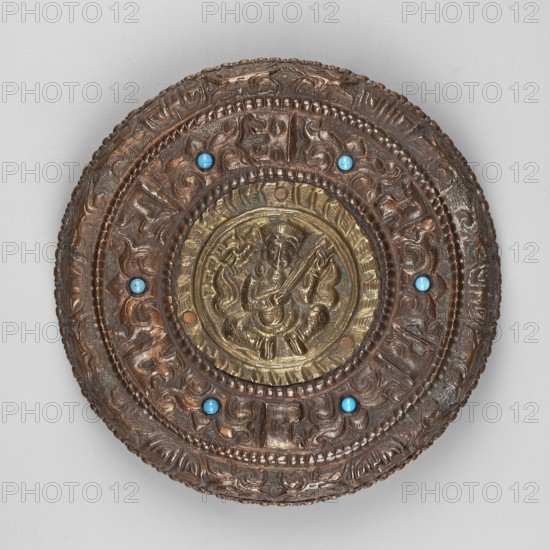Box, Himalayan art, Himalayan culture, 19th/20th century, Tibet, container, height 3.8 cm, diameter 12.6 cm, A round, ornate object with concentric raised bands and intricate carved or cast patterns in brown and gold tones, featuring a central circular medallion with a relief figure and surrounding decorative motifs; the surface includes a few small round turquoise-blue insets placed around the inner band, and the overall colors visible are brown, gold, and turquoise-blue.