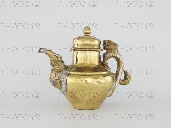 Teapot, Tibetan, 19th century. Jug with a lid on a chain; dragon-shaped handle, spout probably in the shape of a makara. Repoussé copper sheet, tin-plated inside, bronze-plated outside, patinated; silver-plated in sections. Repoussé spout and handle in low relief, inlaid eyes, copper rivets. Cover topped with a lotus bud. Lhasa. Vessel; height 25.5 cm, width 31.0 cm, diameter 19.3 cm, weight 0.85 kg., A gilded metal vessel with a rounded body, tapered base, and a domed lid topped by a pointed finial sits centered against a light gray background. A spout shaped like an animal head projects from one side, showing sculpted facial features and decorative ridges, with a band of silvery ornamentation where it meets the body. The handle on the opposite side is formed like a stylized creature with a curled tail and textured mane, also accented by silvery decorative inlay. The vessel surface shows polished golden tones with areas of subtle sheen and slight surface irregularities. The overall co...