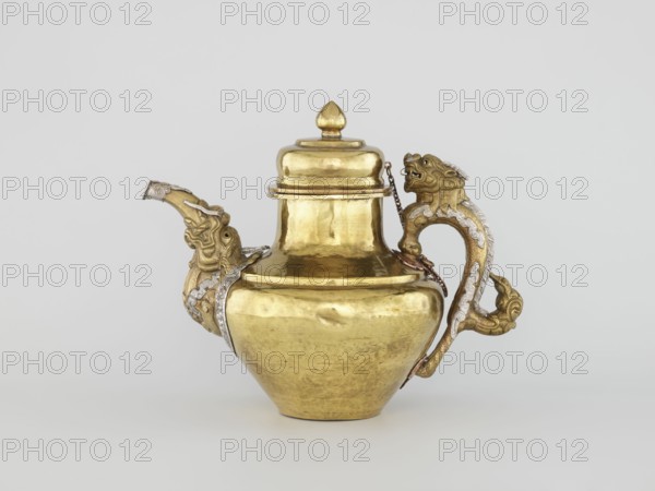 Teapot, Tibetan, 19th century. Jug with a lid on a chain; dragon-shaped handle, spout probably in the shape of a makara. Decorated with dragons, makaras, and lotuses. Repoussé copper sheet, tin-plated inside, bronze-plated outside, patinated; silver-plated in sections. Repoussé spout and handle in low relief, with inlaid eyes and copper rivets. Cover topped with a lotus bud. Lhasa. Vessel; height 25.5 cm, width 31.0 cm, diameter 19.3 cm, weight 0.85 kg., A metal pitcher with a bulbous body and a rounded lid sits against a plain light gray background; the pitcher is primarily golden in color with areas of darker patina and reflective highlights, and it features ornate sculpted elements in matching gold and silvery tones on the spout and handle that resemble stylized animal heads and flowing decorative motifs, with a small chain visible near the lid connecting to the handle.