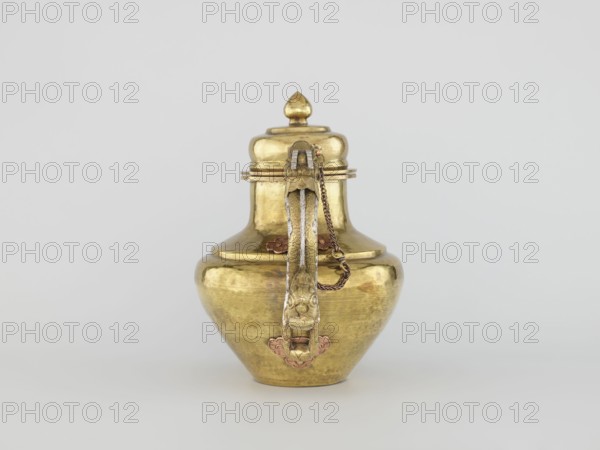 Teapot, Tibetan, 19th century. Jug with a lid on a chain; dragon-shaped handle, spout probably in the shape of a makara. Decorated with dragons, makaras, and lotuses. Repoussé copper sheet, tin-plated inside, bronze-plated outside, patinated; silver-plated in sections. Repoussé spout and handle in low relief with inlaid eyes and copper rivets. Cover topped with a lotus bud. Lhasa. Vessel. Height 25.5 cm; width 31.0 cm; diameter 19.3 cm; weight 0.85 kg., A metallic vessel with a rounded body and a narrow neck topped by a domed lid with a pointed finial sits centered against a pale grey background; the vessel is primarily gold in color with areas of darker patina and subtle reddish accents at decorative fittings, and it features a vertical ornate handle with an attached short chain and decorative mounts, showing reflective surfaces and slight texture from hammering or wear.