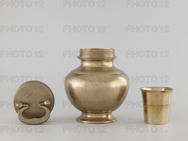 Teapot, gift, art of Southeast Asia, Southeast Asia culture, 19th/20th century, Burma Myanmar, vessel, container, height 22.0 cm, diameter 14.3 cm, A group of three metal vessels displayed on a neutral light-gray surface against a light-gray background: a round lidded container lying on its side with a curved handle and knobs, a bulbous jar with a flared neck and a ridged threaded top standing upright in the center, and a tapered cup with a slightly flared rim on the right; the objects share a metallic gold-brass color with subtle variations in sheen and small areas of darker patina and reflections.