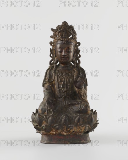 Guanyin, unknown creator; sculptor unknown. Chinese Buddhist bodhisattva figurine on a lotus throne. Qing dynasty, 18th century, China. Sculpture, polychrome/wood material unspecified, height 24 cm. Themes: mercy; Chinese art, Chinese Buddhism., A carved seated figure on a lotus base rendered in dark brown wood with areas of worn gold and reddish-brown showing through, the figure wearing an ornate crown and layered garments with carved necklaces and drapery, a serene facial expression with closed eyes, one hand raised near the chest and the other resting on the knee, the lotus base showing petal shapes with traces of gold and red, set against a plain light gray background.