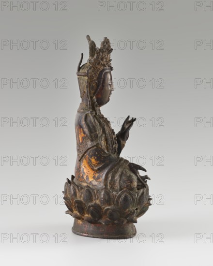 Guanyin; creator, sculptor, Chinese; Qing dynasty 1644–1911, 18th century; Buddhist art; Chinese Buddhism; bodhisattva iconography; mercy; lotus throne iconography; sculpture; height 24 cm., A carved statue of a seated figure on a lotus base, shown in profile facing right, with an ornate crown and detailed jewelry; the figure's hands are held in distinct gestures, and the robes fall in layered folds over the body. The surface shows worn gilding and areas of dark brown and black patina with patches of worn gold and traces of reddish underlayer, and the lotus base appears darker with similar worn gold highlights. The background is a smooth neutral gray that transitions from darker at the top to lighter near the bottom.