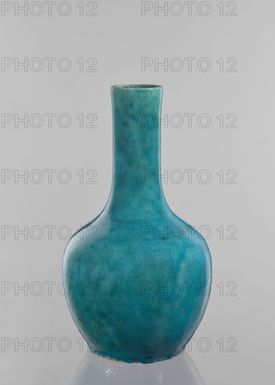 Vase-bottle, crackleware bottle with uniform blue-green glaze and fine cracklework, 19th century China; vessel, height 33 cm, diameter 18 cm., A ceramic vase with a long narrow neck and rounded body sits against a neutral light gray background; the vase is predominantly turquoise with variations of teal and blue-green, showing subtle darker and lighter mottling and a glazed, slightly crackled surface, with a small area of exposed edge at the base and a faint darker spot near the neck.