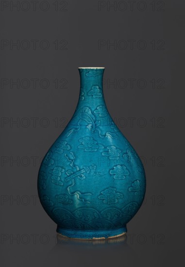 Vase in the shape of an onion-shaped bottle, Chinese art, Chinese culture, Qing 1644–1911 style, hundred antiquities baigu ornament, ceramics. Onion-shaped bottle-vase with a narrow, short neck. The vessel is decorated with a flat relief creating a composition combining a cloud and babao emblems eight precious objects or eight basic symbols. Glaze is single-color, dark, in green-blue tones. 16th–17th century, China. Vessel; height 27 cm; weight 2.6 kg., A teardrop-shaped ceramic vase with a narrow neck and flared rim sits against a dark gray background, the vase surface showing a vibrant turquoise-blue glaze with slightly darker and lighter variations, decorated with an all-over raised pattern of stylized cloud motifs and flowing ribbon-like elements, and a band of repeating wave-like patterns near the base; the rim and foot show a thin exposed edge of unglazed clay in a light beige color, and the vase casts a subtle reflection on the surface beneath it.