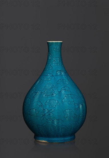 Vase in the shape of an onion-shaped bottle, Chinese, Qing 1644–1911, 16th–17th century, ceramics. Onion-shaped bottle-vase with a narrow, short neck, height 27 cm, weight 2.6 kg. Decorated in flat relief with a composition combining cloud and babao eight precious objects emblems. Single-color dark glaze in green-blue tones., A teardrop-shaped ceramic vase in a vivid turquoise-blue with a narrow neck and flared rim standing against a dark gray background; the vase surface shows an embossed or incised pattern of stylized cloud-like motifs and flowing ribbon shapes, with a band of wave-like decorative patterns near the rounded base, and a small area of exposed lighter clay where the glaze is worn at the bottom edge.