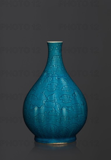 Vase in the shape of an onion-shaped bottle with a narrow, short neck. Onion-shaped bottle-vase decorated in flat relief with a composition combining cloud and babao emblems eight precious objects. Single-color dark green-blue glaze. Ceramics, Chinese, Qing 1644–1911 style; possibly 16th–17th century. Height 27 cm; weight 2.6 kg., A teardrop-shaped ceramic vase with a narrow neck and flared rim sits against a dark gray background, finished in a rich turquoise-blue glaze with a matte, slightly crackled surface; the body is decorated with a repeating raised pattern of stylized cloud-like motifs and flowing ribbon-like lines, with a band of wave patterns circling the lower portion, and a thin unglazed or worn ring of a light beige color visible at the base and rim.
