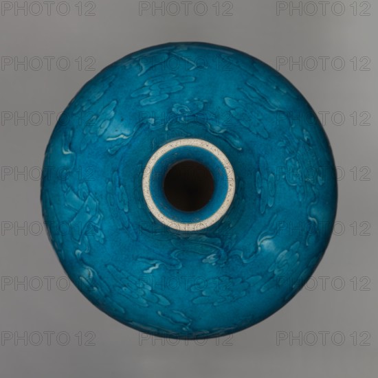 Vase in the shape of an onion-shaped bottle, Chinese, Qing 1644–1911 style, possibly 16th–17th century, onion-shaped bottle-vase with a narrow short neck. Ceramic vessel decorated in low relief combining cloud and babao eight precious emblems. Single-color dark green-blue glaze. Height 27 cm; weight 2.6 kg., A top-down view of a rounded ceramic vessel with a narrow circular opening, showing a bright turquoise blue surface with subtle raised floral and cloud-like patterns, a lighter blue ring around the mouth, and a pale beige rim, all set against a neutral gray background.
