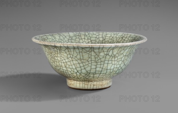 Bowl, ; Chinese; Chinese art; ceramics; Qing 1644–1911, 19th century; bowl supported on a straight, round foot with a flared spout; thick porcelain with grey-celadon glaze and cracklework highlighted by a darker color; vessel; height 11 cm, diameter 25.7 cm, A ceramic bowl shown from the side with a flared rim and a short foot, covered in a crackle glaze with a network of irregular lines; the glaze appears pale green with areas of off-white and subtle beige, and the crackle lines are darker brownish-gray; the interior and exterior share the same crackled pattern, and the bowl sits on a smooth gray surface with a soft shadow beneath it against a mid-gray background.