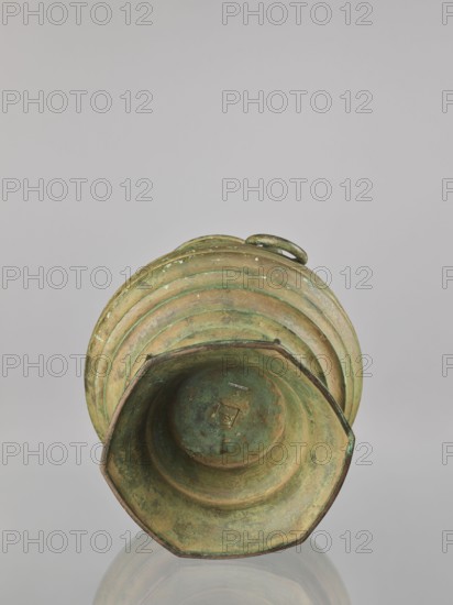 Hu-type vessel hu, bronze wine vessel. Japanese; Meiji–Taisho period, 1st half of the 20th century Meiji 1868–1912 / Taisho 1912–1926. Globular body with narrow, rather high neck and conical stem. Decorated with profiled circles around the body; two mascarons form the handles. Light green artificial patina. Height 40.0 cm. Maker: Hôun craftsman; role/classification. Ceremonial/ritual vessel., An aged metal vessel rests on its side against a neutral background, showing a patina of green and brown with areas of darker verdigris and lighter tan; the vessel has a flared, multi-ridged body with a narrowed neck and a rounded handle at the top edge, and the interior shows concentric stepped rings and irregular surface discoloration in shades of green, brown, and muted gold.