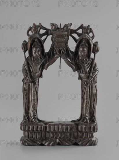 Stand, Chinese, Chinese art, figurative motifs, women, Qing 1644–1911, stand for hanging a gong, 19th century, China, varia, height 45.5 cm, width 29.5 cm, A carved wooden sculpture depicting a symmetrical archway supported by two standing figures facing forward, each wearing ornate headdresses and long robes with carved patterns, holding a long staff topped with a rounded element; the figures have rounded faces with calm expressions and detailed facial features. Above them, carved ornamental elements form a curved top with stylized animal and floral shapes and a central suspended element hanging down from the arch. The base is a carved platform with geometric and leaf-like patterns. The visible colors are dark brown wood tones with subtle lighter brown highlights and faint areas of ochre or tan in carved detailing, set against a neutral light gray background.