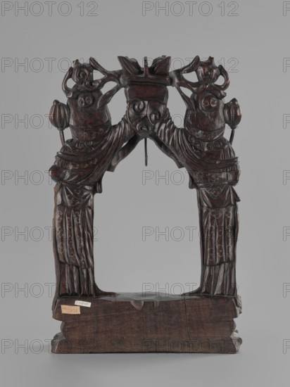 Stand, Chinese, figurative motifs, women, Qing 1644–1911, stand for hanging a gong, 19th century, China, varia; height 45.5 cm, width 29.5 cm, A carved wooden frame with a dark brown finish depicting a symmetrical pair of robed figures facing inward, each holding a rounded object and wearing detailed headdresses, their draped garments showing carved folds and decorative motifs; the figures form an arch supported by a solid rectangular base of the same dark brown wood, with visible grain and a vertical crack on one side; the carving includes rounded facial features and stylized ornamental elements at the top, and the background is a smooth light gray.