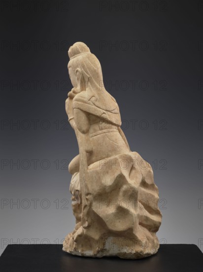 Guanyin with qilin, Chinese, Qing 1644–1911, 19th century, China, sculpture figurine, height 47.5 cm; subject: Guanyin with qilin;, Chinese Buddhist iconography goddess, unicorns., A carved stone figure shown from a rear three-quarter view seated on a textured rock-like base, with long hair gathered into a topknot and draped cloth over the shoulders and back; the figure's arms are bent with hands brought toward the face and one knee raised against the rock. The sculpture has a warm beige and light tan surface with subtle darker beige and brown variations, set against a smooth dark gray to charcoal gradient background and resting on a flat black platform.