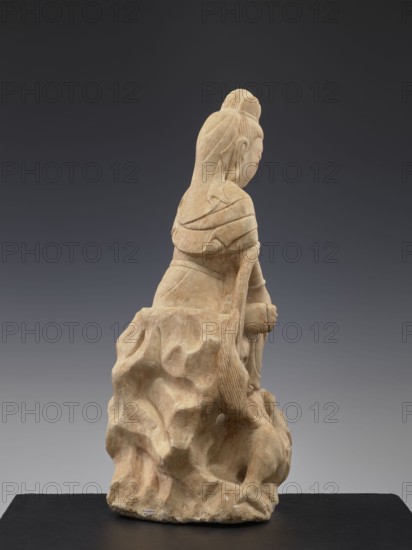 Guanyin with qilin, Chinese, Qing dynasty 1644–1911, 19th century, China, Chinese Buddhism iconography, goddesses, unicorns qilin, sculpture, figurine, height 47.5 cm, A carved stone figure in beige and light tan tones sits on an irregular textured base of the same material, shown from a rear three-quarter view; the figure has long hair pulled into a top knot and a long braided or ribbon-like strand falling down the back, layered clothing with folded drapery across the shoulders and back, and hands held near the front of the body; the stone surface shows smooth and carved grooves, with variations of beige, tan, and hints of brown, set against a neutral dark gray to charcoal background and resting on a flat black platform.