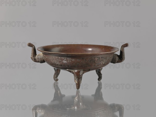 Ding vessel, Ding vessel with three legs and two handles; used for ritual hand washing. Bronze. Japanese, Edo–Meiji period, 19th century Edo period/Meiji period. Height 9.1 cm; width 24.2 cm; diameter 19.6 cm., A shallow round vessel with a reddish-brown bronze surface sits on three ornate tripod legs and features a pair of upward-curving handles shaped like stylized animal heads; the bowl exterior has a band of incised geometric decorative motifs, and the interior shows a smooth, slightly darker patina. The piece rests on a reflective gray surface, and the background is a uniform light gray. Visible colors include reddish-brown, dark brown, gray, and a few darker metallic highlights.