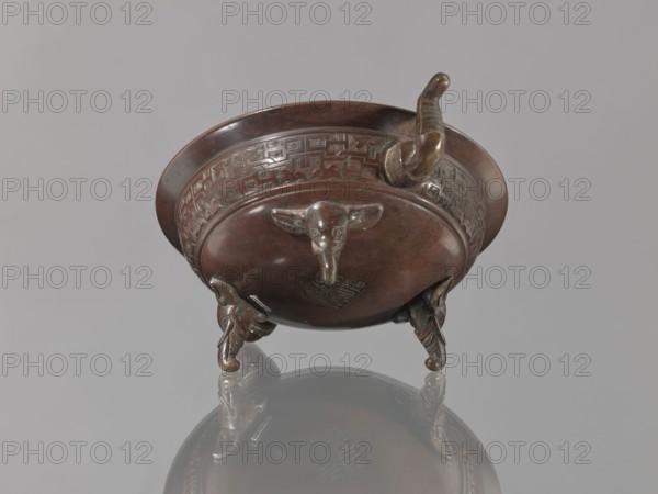 Ding vessel, Ding vessel with three legs and two handles. Used for ritual hand washing. Bronze. Japanese; Edo 1603–1868 / Meiji 1868–1912, 19th century. Height 9.1 cm; width 24.2 cm; diameter 19.6 cm., A bronze vessel with a round body and wide rim sits on a reflective grey surface, showing a polished brown and dark brown patina with greenish highlights in places; the vessel has decorative raised banding around the upper body with geometric motifs, a protruding curved spout or handle, and three sculpted animal-head feet each with curled details; the reflection of the vessel is visible below, and the background is a uniform light grey.