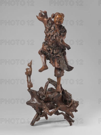 Dancing with a bird, unknown sculptor, birds, cranes, figurative motifs, Asian, dance iconography, Asia, Chinese, 19th century, China place of origin ?, sculpture, height 77 cm, A carved wooden figure of a smiling child with hair in two buns stands with one leg raised on a natural, gnarled wooden base, wearing a textured garment made from knobbly, root-like forms; a small carved bird-like figure perches nearby on a separate small wooden support. The sculpture and base show various brown tones ranging from warm medium brown to darker brown with subtle deeper grain accents, set against a plain light gray background.