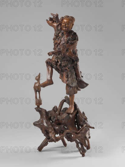 Dancing with a bird; unknown creator sculptor; sculptural work; figurative motifs of birds and cranes; dance iconography; Asian, Chinese culture; 19th century; China place of origin?; sculpture; height 77 cm; provenance noted as purchase., A carved wooden figure of a person standing on an irregular organic base made of knotted, root-like forms, with a carved animal perched on a small support near one raised foot; the person has a smiling expression and textured clothing with flowing, layered details, and one arm raised while the other is bent; the sculpture shows smooth and rough wood surfaces and visible grain, with overall brown and darker brown tones against a neutral gray background.