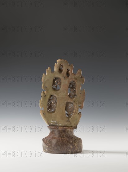 Phoenix with a dragon and a pearl on a base; creator, Chinese; Qing dynasty 1644–1911; 18th century; sculpture/figurine in Chinese art; subjects/icons: phoenix, dragon with a pearl, clouds, rocks; materials: pearls listed, dimensions: height 36.0 cm, width 17.4 cm; function: figurine., A carved object stands on a rounded base, both parts showing mottled brown and green tones; the base is darker brown with lighter speckles and a slightly glossy surface, while the upper carved section is greenish with areas of brownish discoloration. The upper section has an irregular, organic outline with several rounded openings revealing a network of delicate, lacy internal carving visible through the voids, and the edges of this section are uneven and jagged. The lighting creates soft shadows on the smooth surface beneath the object, and the background transitions from dark gray at the top to a lighter gray near the bottom.