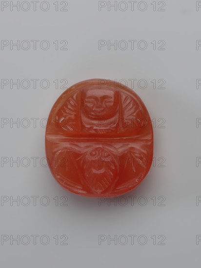 Monk Budai Laughing Buddha and a bat; unknown creator; bats iconography; Chinese art, Chinese culture; Qing dynasty 1644–1911; Budai iconography, Milefo, Maitreya, Buddha of the Future; Oval plaque with a depiction of the deity Budai in the upper part and with a bat in the lower part; 19th century, China; sculpture, plaque; height 2.0 cm, width 1.85 cm, depth 0.65 cm., A small oval object centered on a pale gray background, the object is a translucent orange-red with carved shallow relief showing two stylized faces separated by a horizontal groove, each face framed by geometric leaf-like motifs, the surface is smooth and glossy with subtle highlights and soft shadows around the object's edges.