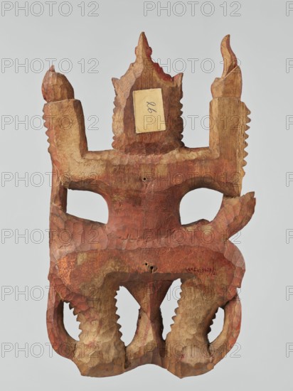 Demon with snakes - wall sculpture, unknown sculptor, snakes, Southeast Asia culture, Southeast Asian art, demons, religion, 19th century, Indonesia, sculpture, height 44.0 cm, width 27.0 cm, A carved wooden mask with a rough, faceted surface and a predominately reddish-brown patina, showing areas of lighter tan wood where the finish is worn or absent, featuring two eye openings and a crown-like top with pointed projections, a pair of raised vertical side elements with serrated edges, and a lower section with curved, scalloped forms and carved tooth-like ridges; the colors visible include reddish-brown, tan, and a few darker brown accents.