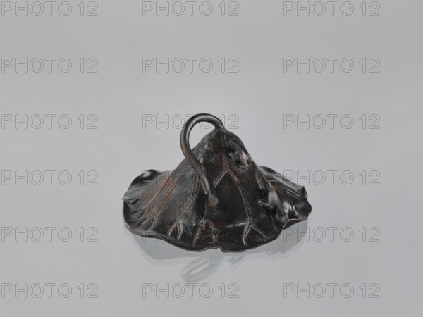 Lotus Leaf with Two Frogs, Ryûbundô,  craftsman author; ; Japanese culture; Japanese art; frogs; paperweight; lotus leaf; Japan; 2nd half of the 19th century; sculpture; height 6.7 cm; width 18.2 cm., A dark brown, slightly glossy sculpted object with an organic, leaf-like shape sits on a pale gray surface, its form spreading outward with visible vein-like ridges and curved edges; a rounded handle-like loop rises from the center, and small raised protrusions appear along one side, with subtle highlights and worn coppery tones on the raised ridges and edges, and a soft reflection of the object visible on the surface beneath it.