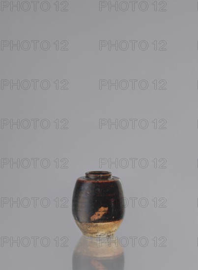 Dried tea container chaire, ; ceramics; chaire vessel; small, barrel-shaped vessel; wheel-thrown grey clay pottery bowl with brown glaze showing rusty and brown shadows; lower unglazed part grey-brown; unsigned; 19th century; Seto, Owari, Japan; function: vessel/container for tea; height 8 cm, diameter 6.2 cm., A small rounded ceramic vessel sits centered on a reflective surface against a plain background; the vessel has a dark glossy upper body showing areas of reddish-brown highlights and a worn lighter base with beige and tan tones, and its reflection is visible beneath it.