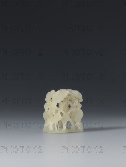 Ornament, Chinese, Ming 1368–1644, Ming style; jade boss ornament depicting bosses, lotuses, headgear, cranes iconography. The ornament presents a complex three-dimensional form: a scene by a lotus pond with four cranes standing in natural poses among densely growing lotuses. The scene was based on an ornament created by thirteenth-century craftsmen during the Yuan era. Mongolian nobility wore wide-brimmed hats with jade bosses on the top; in Ming society that hat style was abandoned, but jade ornaments remained in use and were applied to vessels as decorative elements due to their material and craft value. Early 17th century, China; clothing/varia. Height 3.65 cm, width 3.2 cm, depth 2.5 cm., A pale cream-colored carved object with an openwork, organic form sits on a smooth surface against a dark gray to black gradient background; the object has curved, overlapping elements resembling leaves and stems and casts a soft shadow to the right, and the surface beneath it shows subtle reflec...