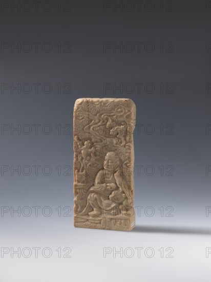 Seal stamp;, bas-relief decoration depicting bats, a lion, and an arhat; Chinese; Qing dynasty 1644–1911, 19th century ; seal stamp in stone; height 20.0 cm, width 9.3 cm, depth 2.9 cm., A rectangular carved stone plaque in shades of beige and tan stands upright against a smooth gradient background of dark gray at the top fading to light gray at the bottom, showing a relief scene with a seated robed figure in the lower center surrounded by flowing cloudlike motifs and other carved details, with subtle variations of brownish-beige on the plaque surface and faint shadowing on the light gray surface beneath it.