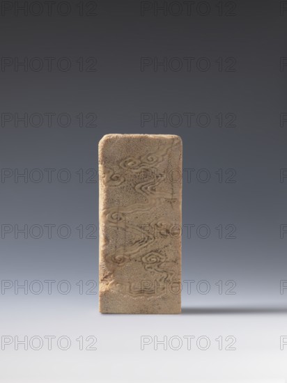 Seal stamp, unknown creator; bats iconography; lion iconography; arhat iconography; Chinese art; seal stamps; Chinese; Qing 1644–1911; bas-relief decoration; 19th century ; China; seal stamp; height 20.0 cm; width 9.3 cm; depth 2.9 cm, A rectangular vertical block with rounded top edges stands alone on a smooth surface, its surface textured and patterned with swirling, cloud-like motifs and fine granular speckles; the block is beige to light brown with slightly darker brown accents in the carved or raised patterns, and it casts a soft shadow to the right on a gradient background that transitions from light gray at the bottom to dark gray at the top.