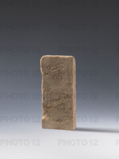 Seal stamp; creator, bats iconography; lion iconography; arhat iconography; Chinese art; seal stamps; Chinese; Qing dynasty 1644–1911; bas-relief decoration; 19th century : China; height 20.0 cm; width 9.3 cm; depth 2.9 cm; inscription: Krieg doctor, A single upright rectangular stone plaque with a rough beige surface stands against a smooth gradient background that transitions from dark gray at the top to pale gray at the bottom; the plaque shows carved swirling cloud-like patterns in a slightly darker beige and tan, with surface pitting and a few worn edges, and it casts a soft shadow to the right on the pale gray ground.