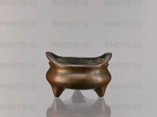 Li-type incense burner, Chinese, Li-type ritual/ceremonial vessel, Ming style Xuande, 1426–1435 with backdated signature reading 1431, Qing style 18th century attribution, ritual use, height 8.8 cm, diameter 14.2 cm., A small three-legged metal vessel with a rounded body and upward-curving rim, showing a patina of brown, bronze, green, and dark gray, sitting on a reflective neutral surface with a pale gray background.