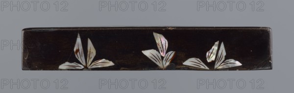 Lid made of black lacquer inlaid with mother-of-pearl, 19th century, Qing dynasty 1644–1911, China; figural scenes with trees and pines; height 1.7 cm, width 11.4 cm, depth 11.4 cm., A long rectangular dark brown object with a smooth surface sits against a gray background, decorated along its front with a few stylized white iridescent leaf shapes that show pink, green, and pale blue flashes and have thin dark brown vein-like markings; the object has slight scuffs and small chips along its edges.