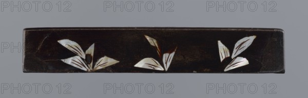 Lid made of black lacquer inlaid with mother-of-pearl, 19th century, China; figural scenes with trees and pines; Qing 1644–1911; height 1.7 cm, width 11.4 cm, depth 11.4 cm;, A long rectangular dark brown object with a smooth surface featuring a group of pale iridescent leaf-like shapes in three clusters spaced along its length, the leaves showing white and cream tones with hints of light brown and subtle reflective sheen; the background beyond the object is a uniform gray.
