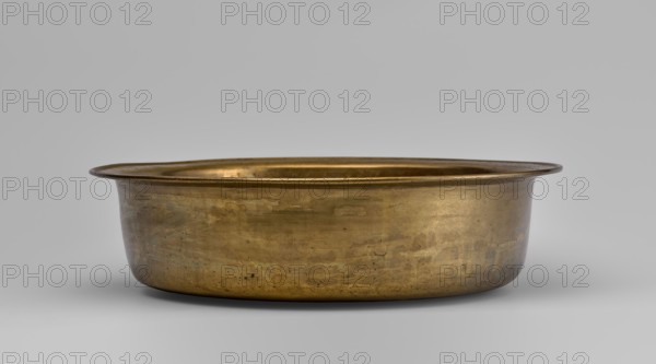 Bowl, round with collar collar decorated with a plant tendril. 19th–20th century, China. Porcelain vessel, height 8.7 cm, diameter 33 cm. Decoration: fruit peaches, pumpkins, pomegranates, lingzhi, images of birds cranes, deer, pine trees, artemisia, plant ornament; Chinese symbols for happiness., A shallow round metal basin with a wide flared rim sits centered against a smooth neutral background; the basin has a warm golden-bronze color with areas of darker patina and subtle greenish and brownish discoloration, visible surface scratches, and small patches of wear; the interior rim shows a slightly brighter golden tone while the exterior surface displays mottled variations in sheen and texture.