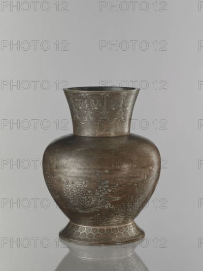 Vase, Ovoid, bulbous vase made of a pewter alloy, on a wide base with a wide, flared neck. Engraved decoration inlaid with a thin layer of silver: cranes among reeds by the water; a symmetrically repeated floral motif on the neck. Kikko pattern, grasses, birds, water, cranes iconography. Japanese, Meiji period 1868–1912, 19th/20th century. Vessel. Height 30.1 cm; diameter 15.6 cm., A rounded metal vase with a flared neck sits against a pale gray background, showing a dark bronze-brown surface with areas of lighter metallic sheen and subtle greenish patina; the flared rim area features engraved decorative panels with repeating leaf-like motifs in a lighter metallic tone, the bulbous body displays delicate engraved scenes of foliage and grasses in a pale metallic contrast, and the slightly flared foot has a geometric honeycomb-like pattern in similar bronze and lighter metallic colors, with a soft reflection visible beneath the vase.