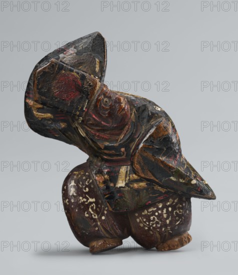 Netsuke in the shape of a sanbasô dancer; sculptor, Japanese, Edo period 18th century; ivory or wood figurine netsuke; depicts a dancer wearing a mask used in ritual dance; height 6.3 cm, width 4.0 cm., A small carved wooden figure painted in black, brown, red, gold, and white tones, shown against a plain light gray background, with visible wear and flaked paint; the figure has a rounded body and squat legs with decorative white markings, a head turned to the side with carved facial features and layered painted patterns, and broad, winglike or cloak elements wrapping around the upper body with traces of red and gold highlights.