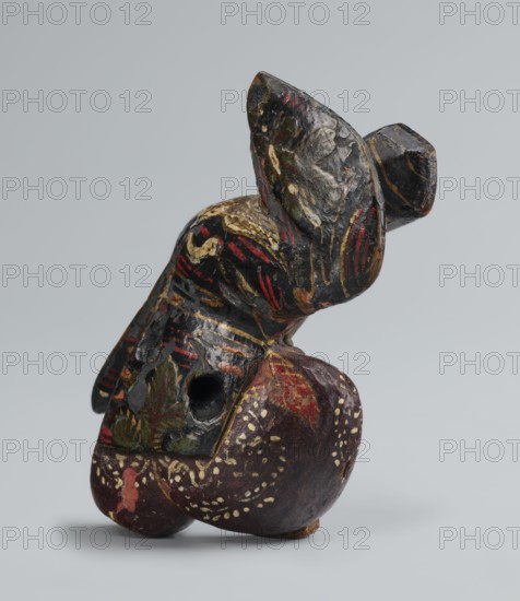 Netsuke in the shape of a sanbasô dancer, Japanese, Edo period 18th century, netsuke figurine depicting a dancer with mask, carved, height 6.3 cm, width 4.0 cm., A carved, painted object with an abstract, rounded form resting on a flat surface, showing a worn, textured surface and a visible hollow hole; the piece displays a palette of black, dark brown, deep red, muted gold, and small areas of green, with decorative strokes and speckled dots in gold and cream, and patches where paint is chipped revealing darker underlying tones.