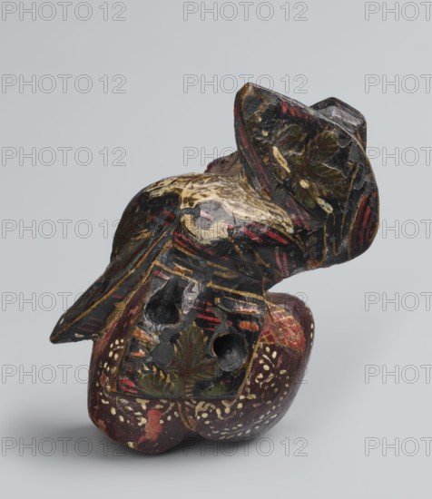Netsuke in the shape of a sanbasô dancer;, Japanese, Edo period 18th century; netsuke figurine depicting a ritual dancer wearing a mask; height 6.3 cm, width 4.0 cm., A carved object with a worn, painted surface sits against a pale gray background; the object shows a mix of dark colors including black and deep red, with visible areas of gold, green, and cream; sections of the paint appear chipped and scuffed, revealing lighter and darker underlying tones; the form includes rounded and angular shapes with carved depressions and holes, and decorative leaf-like motifs and short linear strokes in red and gold across its surface; small clusters of cream-colored dot marks decorate part of the lower area, and traces of uneven texture and brushwork are visible where the paint has worn away.