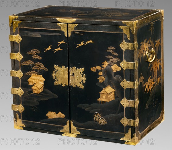 Small cabinet kodansu, Meiji period 2nd half of the 19th century, Japan. Rectangular cabinet closed with double doors mounted on engraved brass hinges; equipped with seven drawers the eighth at the very top is missing. Door face filled with a landscape composition of pavilions by the water, hills, and a flock of cranes. Side exterior walls decorated with a bamboo motif; interior decorated with floral motifs. Wood coated with black lacquer; decorative motifs executed in maki-e with gold powder. Motifs include flowers, landscape elements, geese, mountains, pines, bamboo, spotted pheasants, and architecture. Piece of furniture. Height 45.5 cm, width 52.2 cm, depth 31.7 cm., A rectangular black lacquered cabinet with ornamental metal corner protectors and hinges in a gold tone, decorated with gold-colored landscape scenes including stylized trees, small raised buildings on stilts, flying birds, and bamboo stalks, with a gold ring handle on one side; the cabinet shows wear at some edges rev...