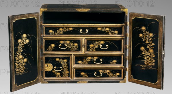 Small cabinet kodansu, Meiji period 2nd half of 19th century, Japan. Rectangular cabinet closed with double doors mounted on engraved brass hinges; equipped with seven drawers the eighth at the top is missing. Door face filled with a landscape composition with pavilions by the water, hills, and a flock of cranes. Side exterior walls decorated with a bamboo motif; interior decorated with floral motifs. Decoration executed in maki-e with gold powder on wood coated with black lacquer. Motifs include flowers, landscape elements, geese, mountains, pines, bamboo, spotted pheasants, and architecture. Piece of furniture; height 45.5 cm, width 52.2 cm, depth 31.7 cm., A rectangular black cabinet with its two doors open to reveal a set of drawers decorated with gold floral motifs; the exterior and drawer faces are glossy black with gold trim and gold handles, and the inner panels of each door feature vertical gold plant designs on a black background framed by a gold border; the drawer fronts dis...