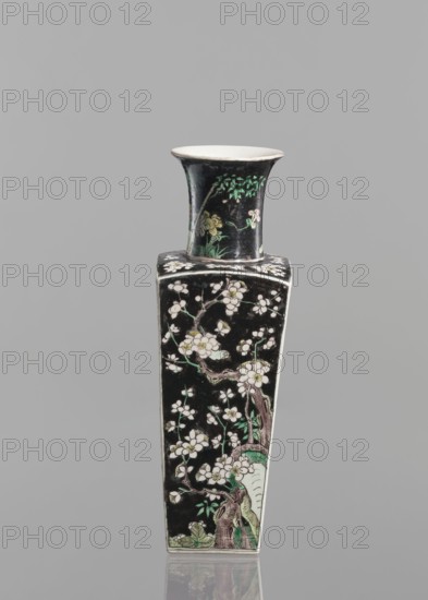 Vase;, Chinese; Qing dynasty 1644–1911; 18th century; colored porcelain famille noire with floral decorations depicting plum trees and birds; vessel; height 22.5 cm., A tall, narrow vase with a flared rim sits against a plain gray background; the vase has a predominantly black surface decorated with floral and tree motifs in white, pale pink, green, pale yellow, and brown, showing branches, blossoms, leaves, and sections of a tree trunk, with the rim interior appearing white and the overall shape transitioning from a square-bodied lower section to a slightly flared circular neck.